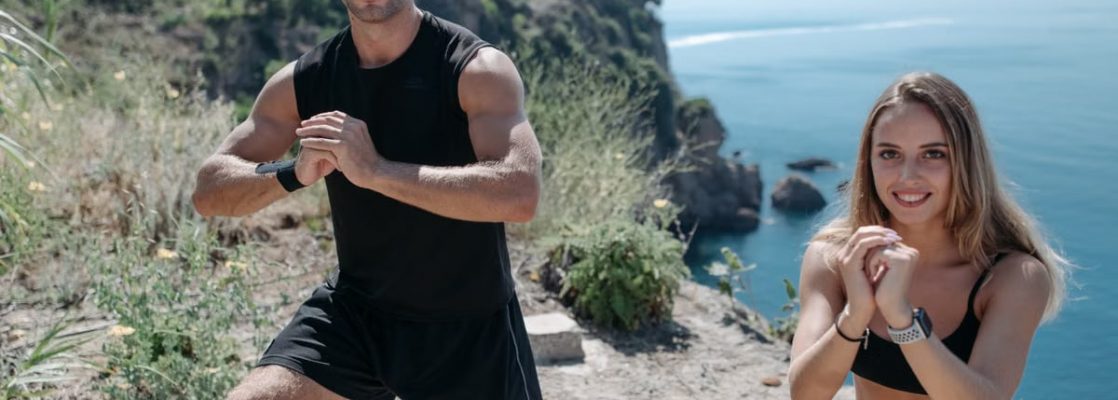 A couple performs fitness exercises on a cliff with a scenic sea view, promoting healthy living.